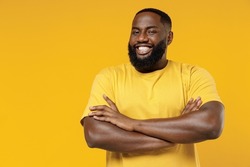 Young smiling cheerful satisfied positive happy black man 20s wear bright casual t-shirt hold hands crossed folded isolated on plain yellow color background studio portrait. People lifestyle concept