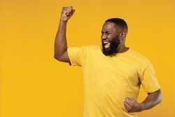 Young exultant happy black man 20s in bright casual t-shirt doing winner gesture celebrate clenching fists say yes isolated on plain yellow color background studio portrait. People lifestyle concept