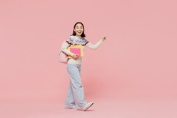 Full body amazed teen student girl of Asian ethnicity in sweater hold backpack point index finger aside on workspace area isolated on pastel plain light pink background Education in university concept