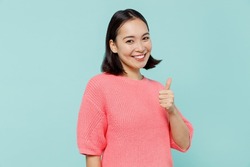 Young smiling fun happy woman of Asian ethnicity 20s wearing pink sweater showing thumb up like gesture isolated on pastel plain light blue color background studio portrait. People lifestyle concept