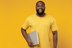 Young cheerful copywriter fun happy black man 20s wearing bright casual t-shirt hold use closed laptop pc computer isolated on plain yellow color background studio portrait. People lifestyle concept