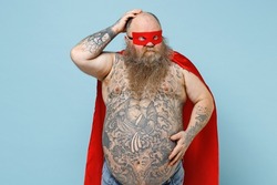 Caucasian puzzled confused fun fat pudge obese chubby overweight blue-eyed bearded man 30s wearing red cartoon character cloak mask hold belly scratch head isolated on pastel blue background studio