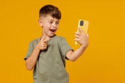 Little small smiling boy 6-7 years old in green t-shirt doing selfie shot on mobile cell phone point finger on camera isolated on plain yellow background. Mother's Day love family lifestyle concept