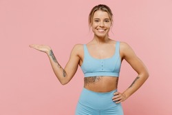 Young strong sporty athletic fitness trainer instructor woman wear blue tracksuit spend time in home gym show empty palm isolated on pastel plain light pink background Workout sport motivation concept