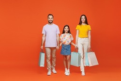 Full body young happy parents mom dad with child kid daughter teen girl in basic t-shirts hold package bags with purchases after shopping show thumb up isolated on yellow background Family day concept