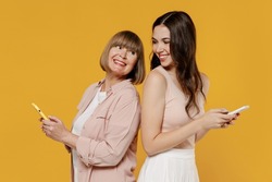 Side view two fun young daughter mother together couple women in casual clothes hold mobile cell phone stand back to back look to each other isolated on plain yellow background studio Family concept