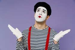 Confused preoccupied pensive perplexed young mime man with white face mask wears striped shirt beret spreading hands looking up above isolated on plain pastel light violet background studio portrait