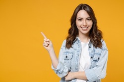 Young smiling woman promoter in denim shirt white t-shirt recommend suggest select advert point index finger aside on workspace commercial promo area mock up copy space isolated on yellow background