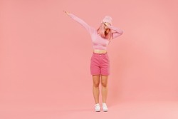Full body young woman 20s with bright dyed rose hair in rosy top shirt hat doing dab hip hop dance hands move gesture isolated on plain light pastel pink background. People lifestyle fashion concept