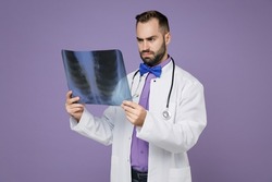 Puzzled young bearded doctor man in medical gown stethoscope hold X-ray of lungs fluorography roentgen isolated on violet background studio portrait. Healthcare personnel health medicine concept