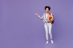 Full body young girl woman of African American ethnicity teen student in shirt point index finger aside on workspace area isolated on plain purple background. Education in university college concept