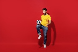Full size body length young bearded man football fan in yellow t-shirt cheer up support favorite team juggling soccer ball isolated on plain dark red background studio portrait. Sport leisure concept