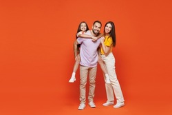 Full size young fun happy parents mom dad with child kid daughter teen girl in basic t-shirts giving piggyback to daughter isolated on yellow background studio Family day parenthood childhood concept.
