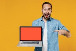 Young shocked happy freelancer copywriter man 20s wear blue shirt hold use work point finger on laptop pc computer with blank screen workspace area isolated on plain yellow background studio portrait.