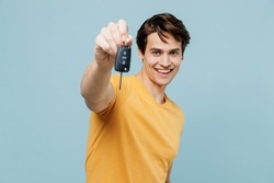 Young happy smiling satisfied cheerful caucasian man 20s in yellow t-shirt holding give car keys keyless system isolated on plain pastel light blue background studio portrait. People lifestyle concept