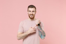 Excited young bearded tattooed man in pastel casual t-shirt wearing smart watch on hand isolated on pink background studio portrait. People lifestyle concept. Mock up copy space. Tattoo translate fun