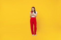 Full size body length smiling fun young girl woman of Asian ethnicity 20s years old wears casual clothes hold in hand use mobile cell phone send sms isolated on plain yellow background studio portrait