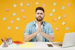 Young asking pleaded employee business man in shirt sit work at white office desk with pc laptop hands folded in prayer gesture, begging about something isolated on yellow background studio portrait.