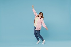 Full length young fun joyful smiling redhead chubby overweight woman 30s wearing in pink shirt jeans leaning back stand on toes with oustretched hands hands dance isolated on pastel blue background