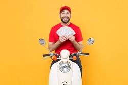 Delivery man in red cap t-shirt uniform driving moped motorbike scooter hold cash money isolated on yellow background studio Guy employee working courier Service quarantine pandemic covid-19 concept.