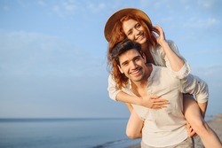 Young cheerful happy couple two friends family man woman in white clothes boyfriend give piggyback ride to joyful, girlfriend sit on back at sunrise over sea beach ocean outdoor seaside in summer day