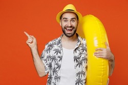 Young surprised tourist man in beach shirt hat hold inflatable ring point index finger aside on workspace isolated on plain orange background studio portrait. Summer vacation sea rest sun tan concept