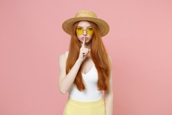 Young redhead woman 20s ginger long hair in straw hat glasses summer clothes secret woman say hush be quiet with finger on lips shhh gesture wish isolated on pastel pink background studio portrait.