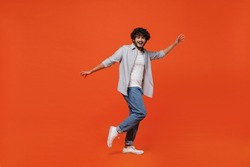 Full size body length side profile view jubilant young bearded Indian man 20s years old wears blue shirt dance waving fooling around have fun enjoy isolated on plain orange background studio portrait