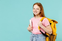 Little smart happy pupil redhead kid girl 12-13 year old in pink striped t-shirt hold notebook book yellow school bag backpack isolated on pastel blue background Children lifestyle childhood concept
