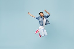 Full size happy exultant little kid teen girl of African American ethnicity 12-13 year old in denim jacket jump high stretch hands isolated on pastel plain light blue background. Childhood concept.