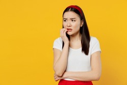 Nervous disturb young sad woman of Asian ethnicity 20s years old wears white t-shirt looking aside biting nails isolated on plain yellow background studio portrait. People emotions lifestyle concept