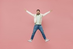 Full body young overjoyed exultant jubilant happy fun man 20s in trendy jacket shirt jump high with outstretched hands isolated on plain pastel light pink background studio. People lifestyle concept