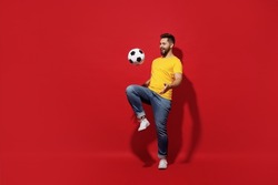 Full size body length overjoyed excited jubilant fun young bearded man football fan in yellow t-shirt juggling soccer ball isolated on plain dark red background studio portrait. Sport leisure concept