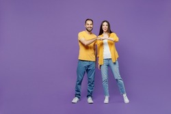 Full body young smiling happy couple two friends family man woman together in yellow casual clothes looking camera giving a fist bump in agreement isolated on plain violet background studio portrait