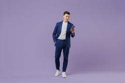 Full size young successful employee business man lawyer 20s wear formal blue suit white t-shirt move stroll hold use mobile cell phone hand in pocket isolated pastel purple background studio portrait