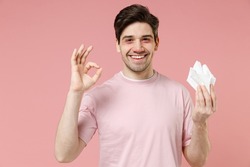 Sick ill ailing allergic man has red eyes runny nose suffer from allergy hold paper napkin isolated on pastel pink color wall background studio Healthy lifestyle disease treatment cold season concept