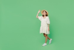 Full body side view young happy smiling fun cheerful woman she 20s wear white dress hat walking go waving hand isolated on plain pastel light green background studio portrait. People lifestyle concept