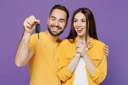 Young smiling satisfied happy fun couple two friends family man woman together wear yellow clothes looking camera hold car key fob keyless system isolated on plain violet background studio portrait