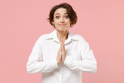 Young asking employee business woman corporate lawyer in classic formal white shirt work in office hands folded in prayer gesture, begging about something isolated on pastel pink background studio.