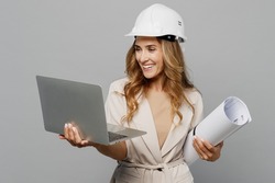 Young architect engineer designer employee white woman wear pastel clothes hardhat hold blueprints use laptop pc computer isolated on plain light grey background. People work on architecture project