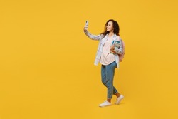 Full body young black teen girl student she wear casual clothes backpack bag hold books do selfie shot on mobile cell phone isolated on plain yellow background. High school university college concept