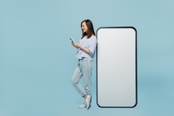 Full body young happy woman she 20s in casual blouse big huge blank screen mobile cell phone with workspace copy space mockup area hold smartphone isolated on pastel plain light blue background studio