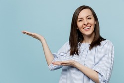 Young happy smiling woman she 20s in casual blouse indicate point hands arms aside on workspace area mock up isolated on pastel plain light blue background studio portrait. People lifestyle concept