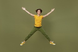 Full body young exultant fun happy woman she 20s wear yellow t-shirt jump high with outstretched hands legs like flying in air isolated on plain olive green khaki background. People lifestyle concept
