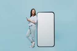 Full size young happy woman she 20s in casual blouse big huge blank screen mobile cell phone with workspace copy space mockup area hold smartphone isolated on pastel plain light blue background studio