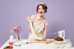 Young happy housewife housekeeper cook chef baker woman in pink apron work at table kitchenware kneads dough baking isolated on violet background studio portrait Process cooking food pastry concept.