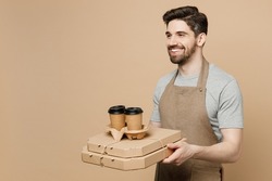 Young fun man barista barman employee in brown apron work in coffee shop hold italian pizza in cardboard flatbox tea cup isolated on plain pastel light beige background Small business startup concept