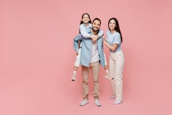 Full body young parents mom dad with child kid daughter teen girl in blue clothes giving piggyback ride to kid, sit on back isolated on plain pastel light pink background Family day childhood concept