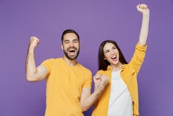 Young overjoyed excited couple two friends family man woman together in yellow casual clothes doing winner gesture celebrate clench fists say yes isolated on plain violet background studio portrait