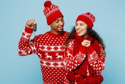 Merry young couple two man woman wear red Christmas sweater Santa hat posing give gift car keys fob keyless system isolated on plain pastel light blue background. Happy New Year 2023 holiday concept